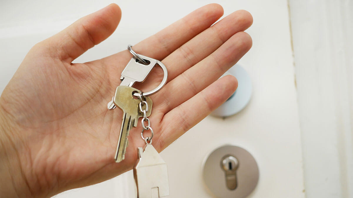 Person holing house key from the home they're selling with white entrance door in the background